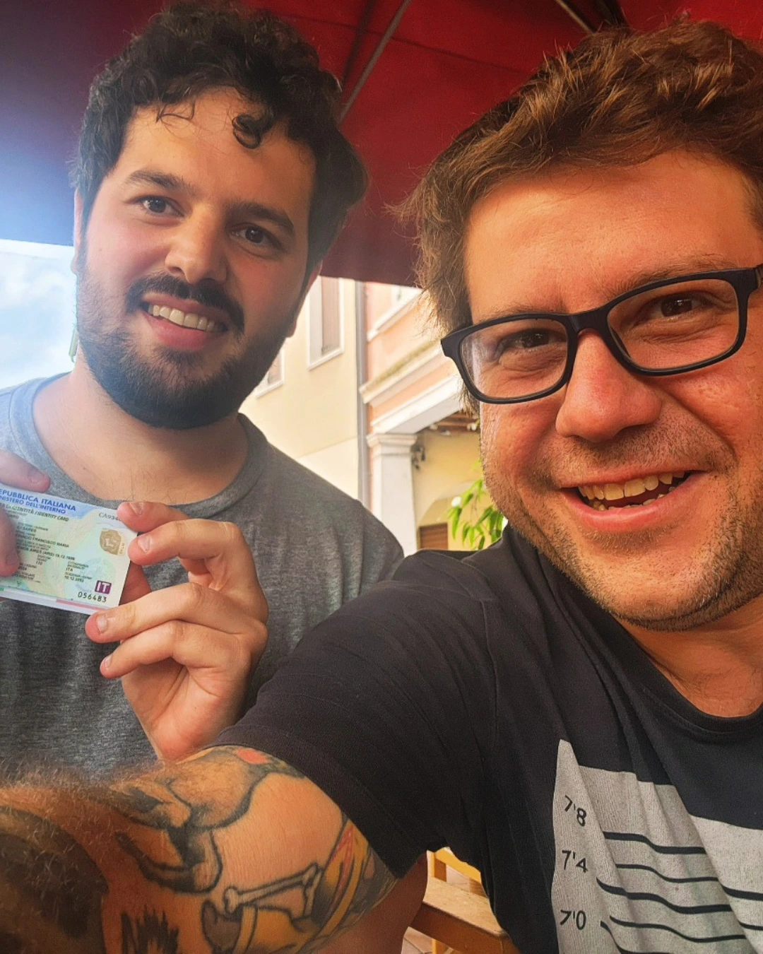 Dos clientes de Speranza sonriendo juntos, uno con el documento de identidad italiano